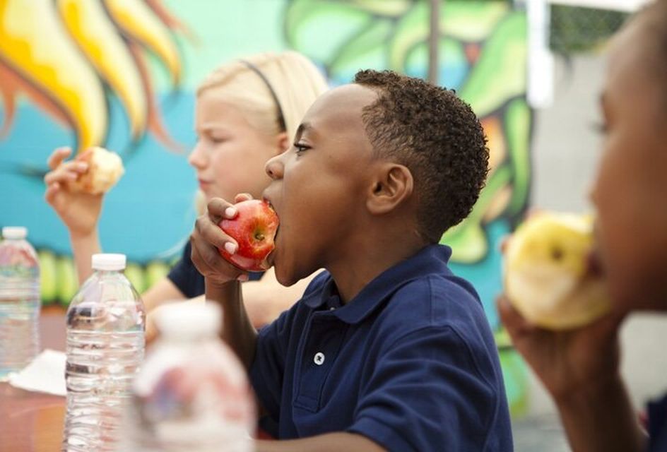 A young black boy in a blue polo shirt eating an apple