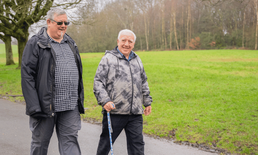 Two older man walking in a park on a wintery day while smiling.