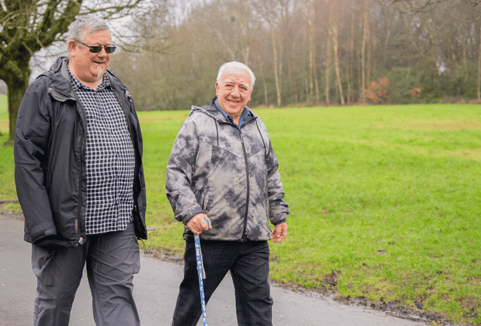 Two older man walking in a park on a wintery day while smiling.