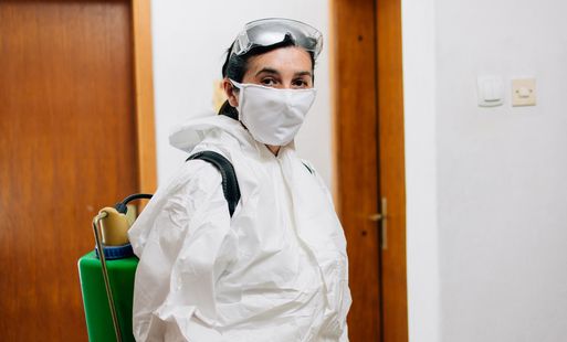 A female pest controller wearing protective clothing and a face mask
