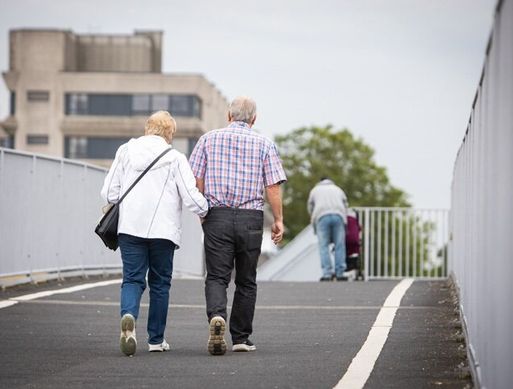 An elderly couple walk across a pedestrian bridge.