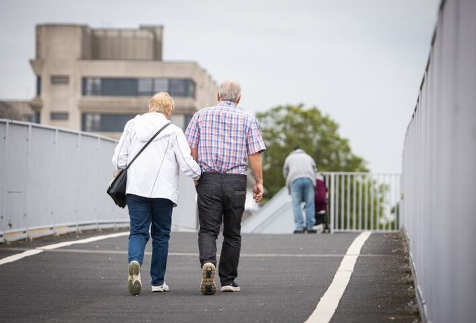 An elderly couple walk across a pedestrian bridge.