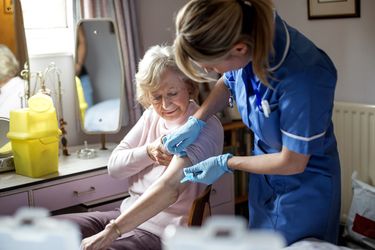 A nurse places a plaster over an elderly woman's arm.