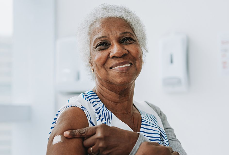 Older women smiling pointing at plaster on arm having just been vaccinated.