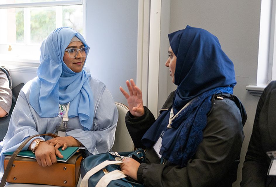 Two women talking at an RSPH event. One wears a pale blue hijab and glasses and the other wears a navy blue hijab.
