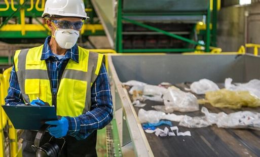 A man in a hard hat, high vis jacket, protective gloves and face mask surveys a recycling centre.