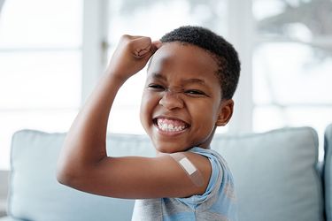 Young boy with plaster on his arm cheering with happiness after getting a vaccination