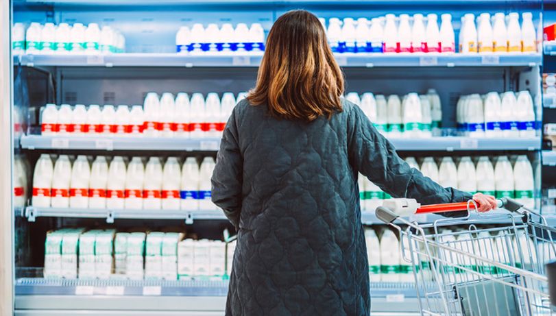 Woman looking at milk in a supermarket cooler, thinking about the price of everyday products