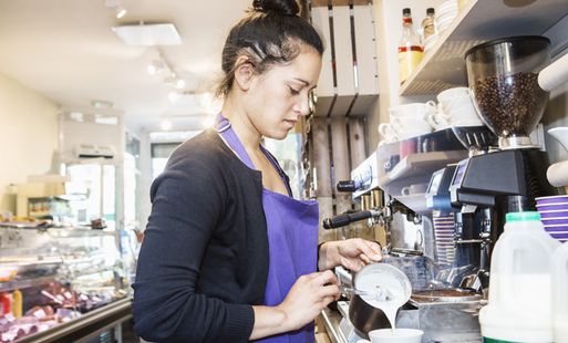 A female barista pours milk into a cup in a cafe.