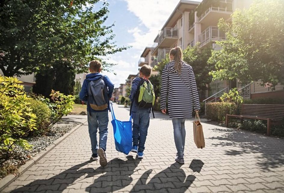 Two young boys carry a plastic bag down a street with their mother