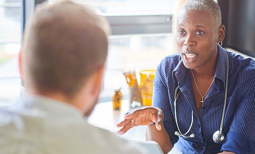 NHS doctor sitting down wearing a stethoscope calmly explaining something to a patient.