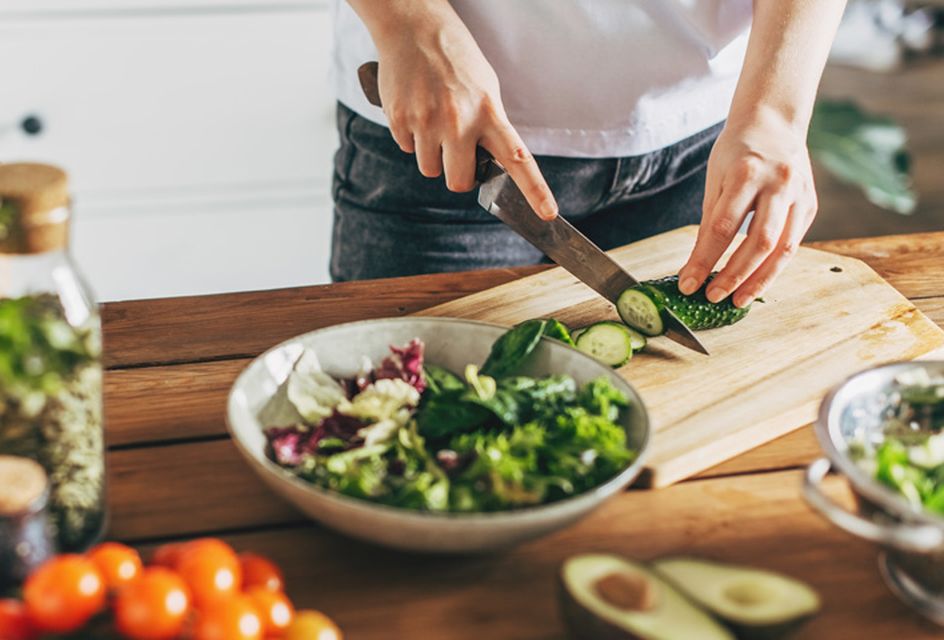 Someone chopping a cucumber on a chopping board in a kitchen