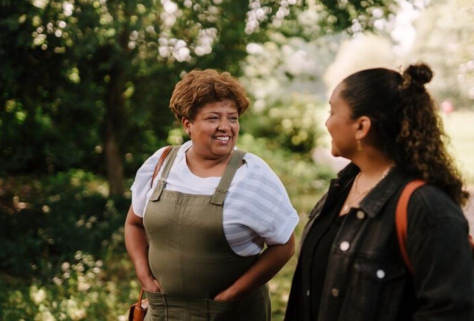 Two women are walking through a park smiling.