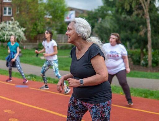An elderly white woman exercises in a park with others