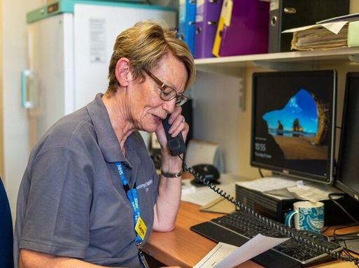 A white woman with short hair speaks on the phone in an office.