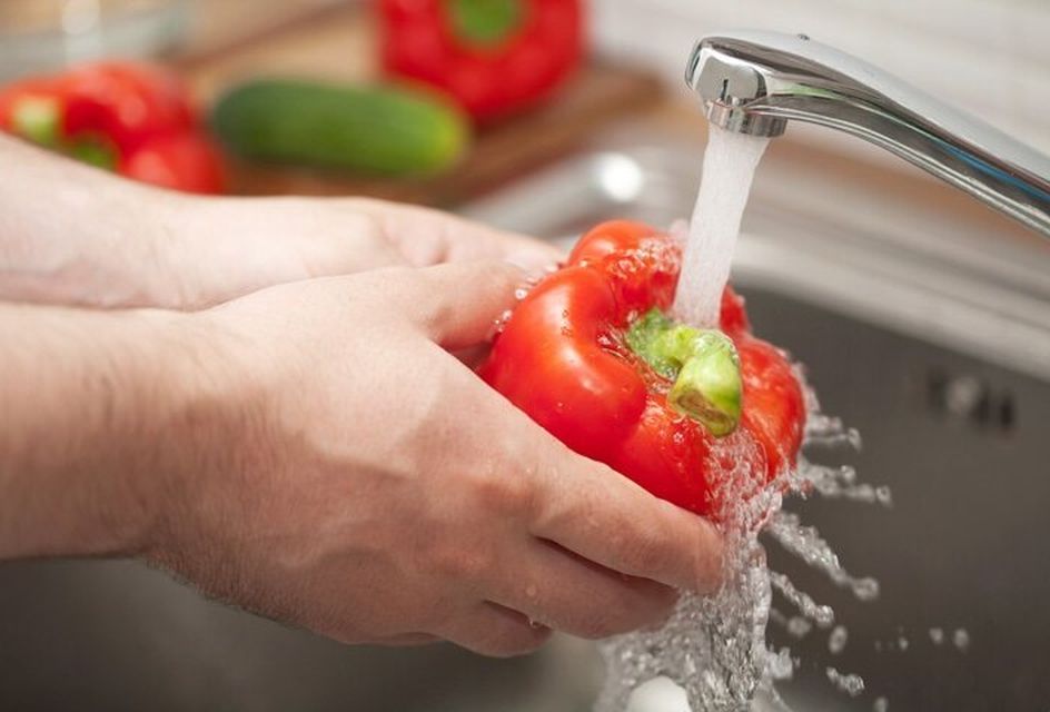 Someone washing a red pepper under a running tap